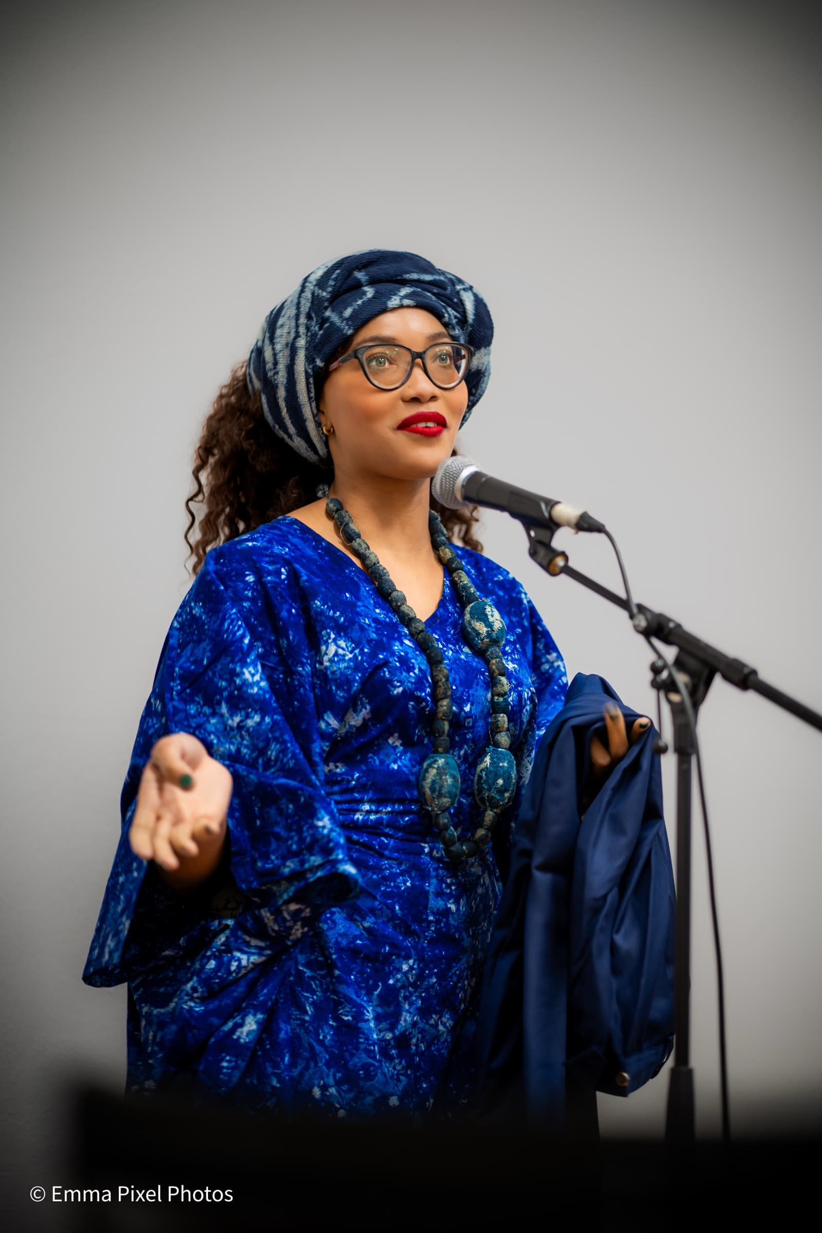 Woman speaking at a microphone, indigo dress and headwrap