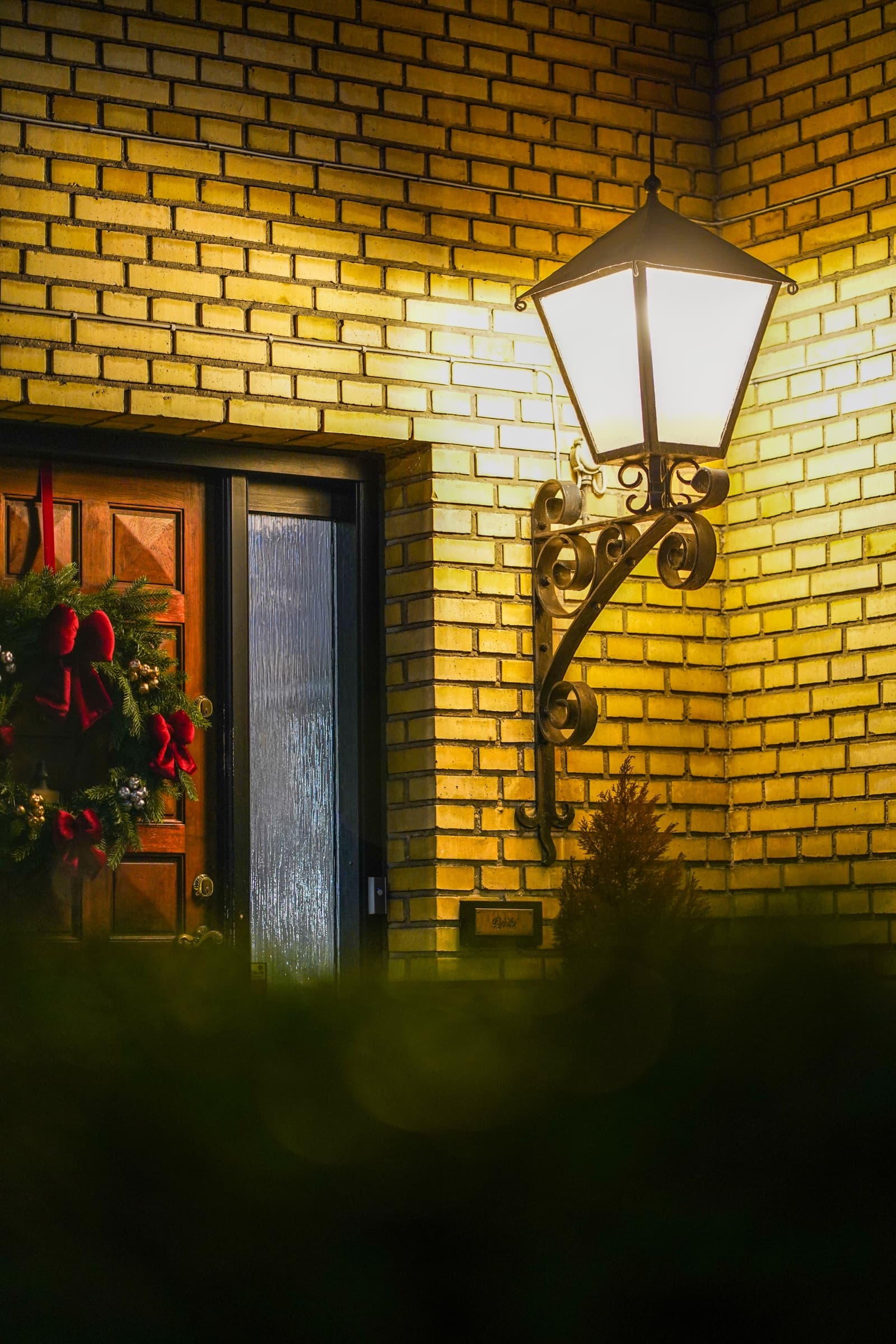Festive front door with wreath and lantern, yellow brick at night