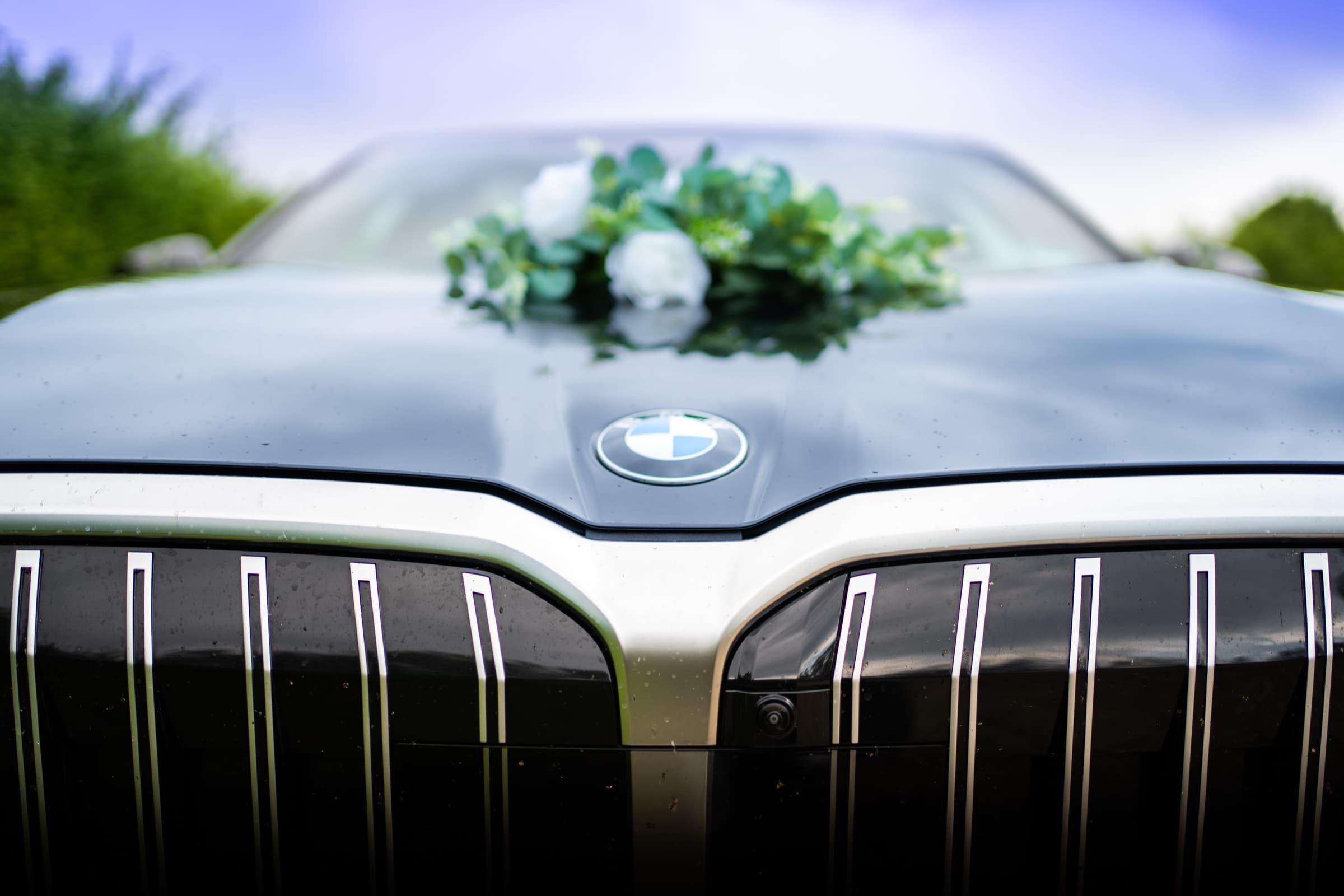 White rose and eucalyptus arrangement on a wedding car hood, BMW emblem framed below