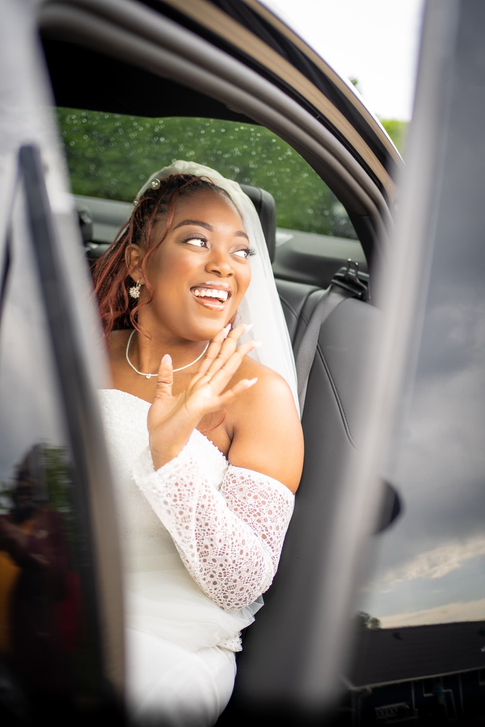 Bride mid-laugh through the rear window of the wedding car, hand near her cheek
