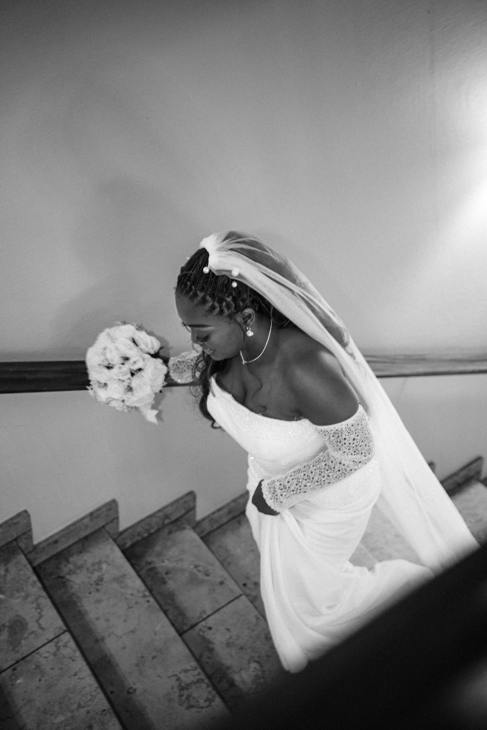 Bride descending a stone stairway, veil trailing behind, black-and-white