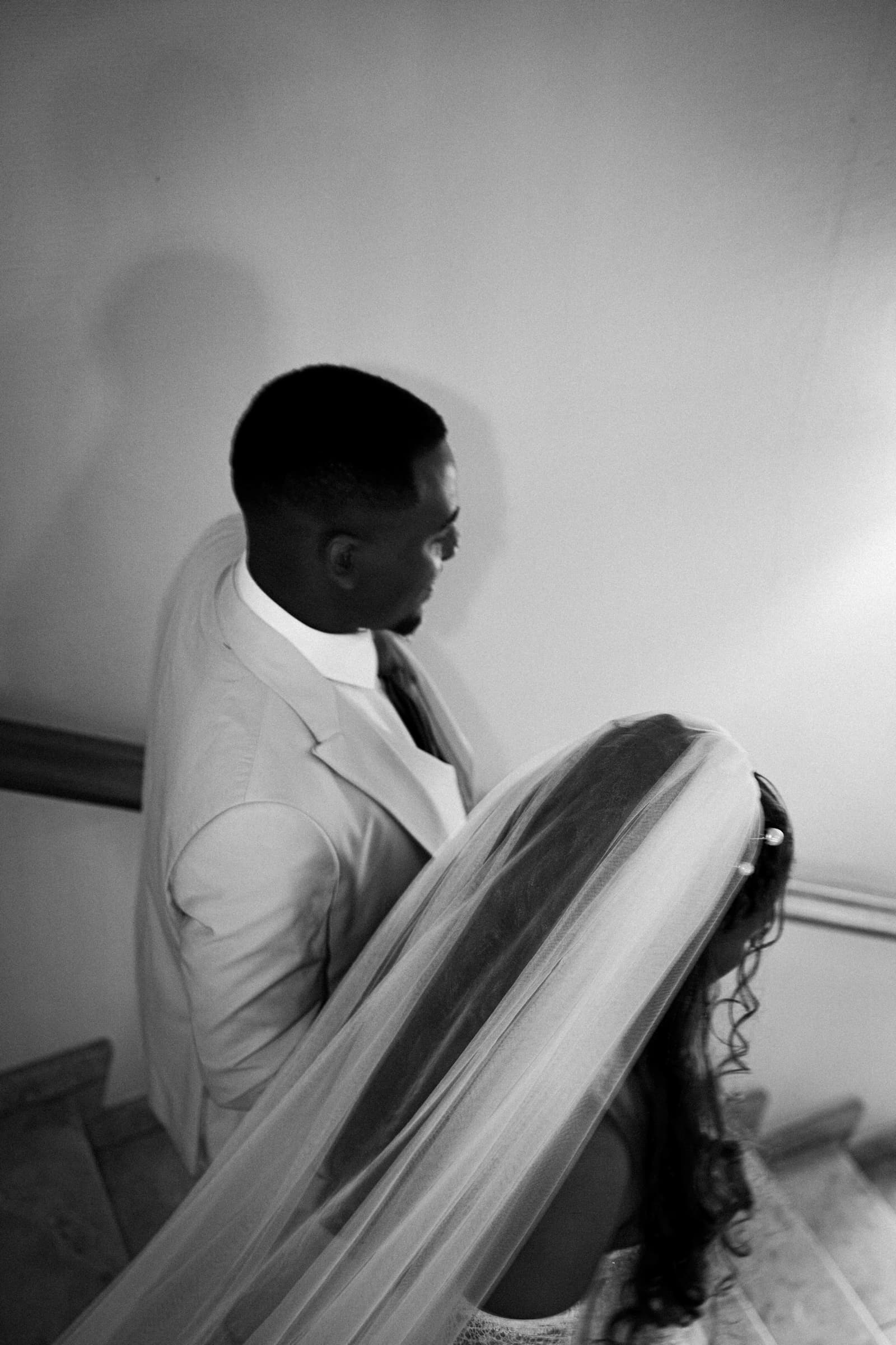 Groom in profile while the bride's veil drifts across the frame, black-and-white