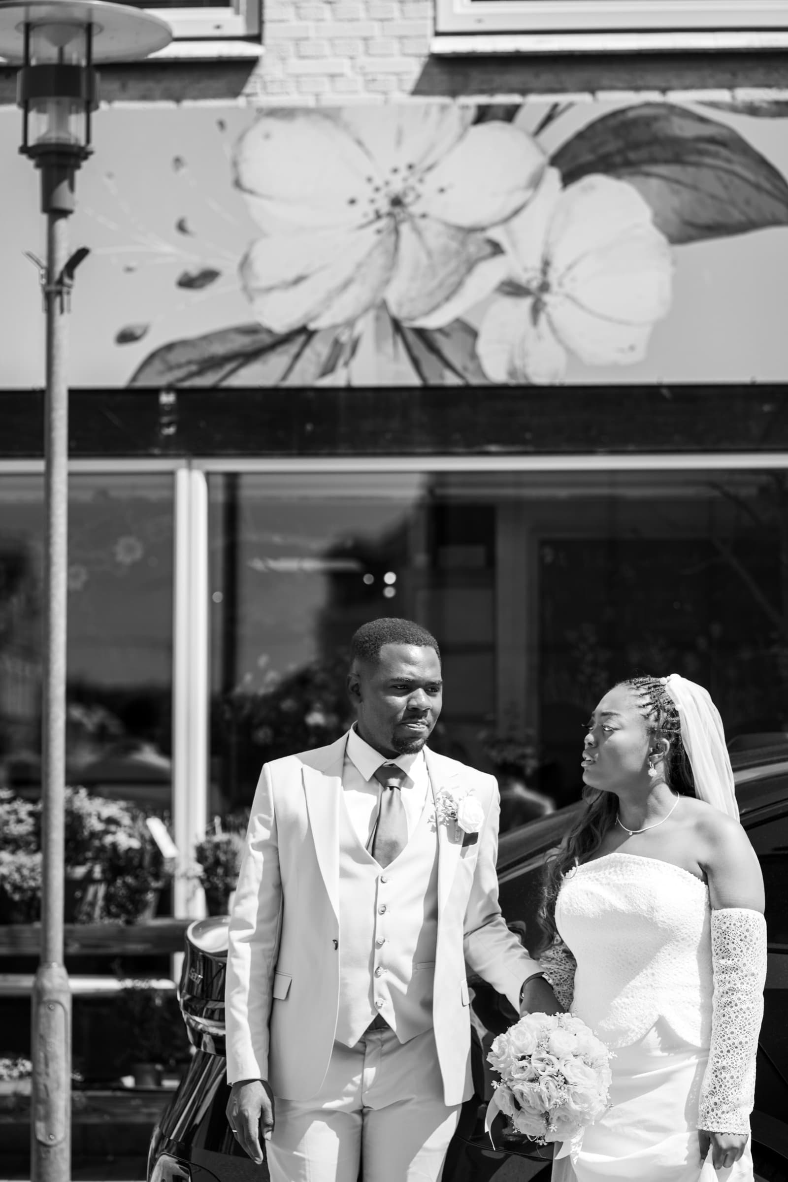 Couple beside a painted flower mural on a sunlit street, black-and-white
