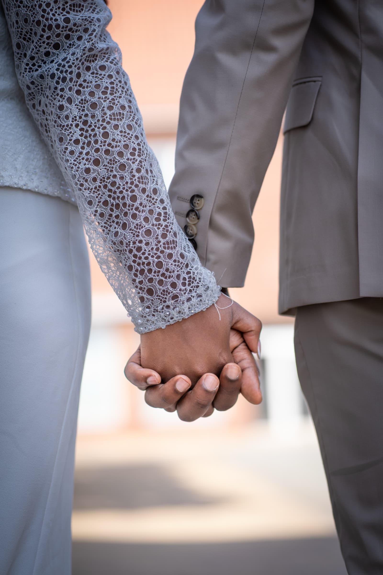 Bride and groom's hands clasped, lace cuff against wool sleeve, quiet detail