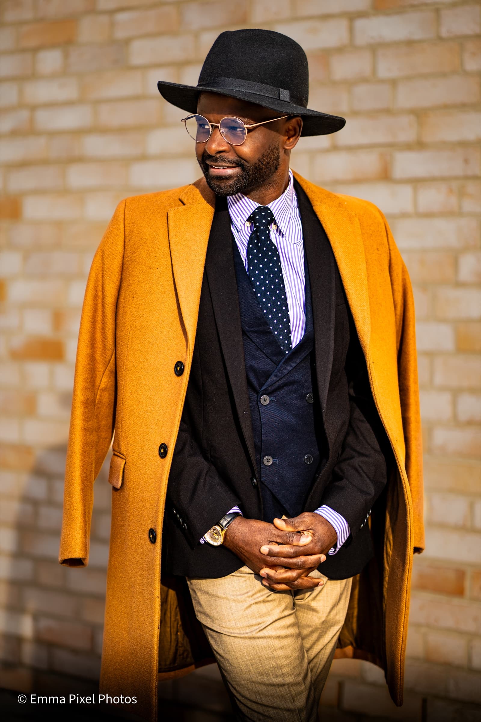 Mustard wool coat and black fedora against a brick wall
