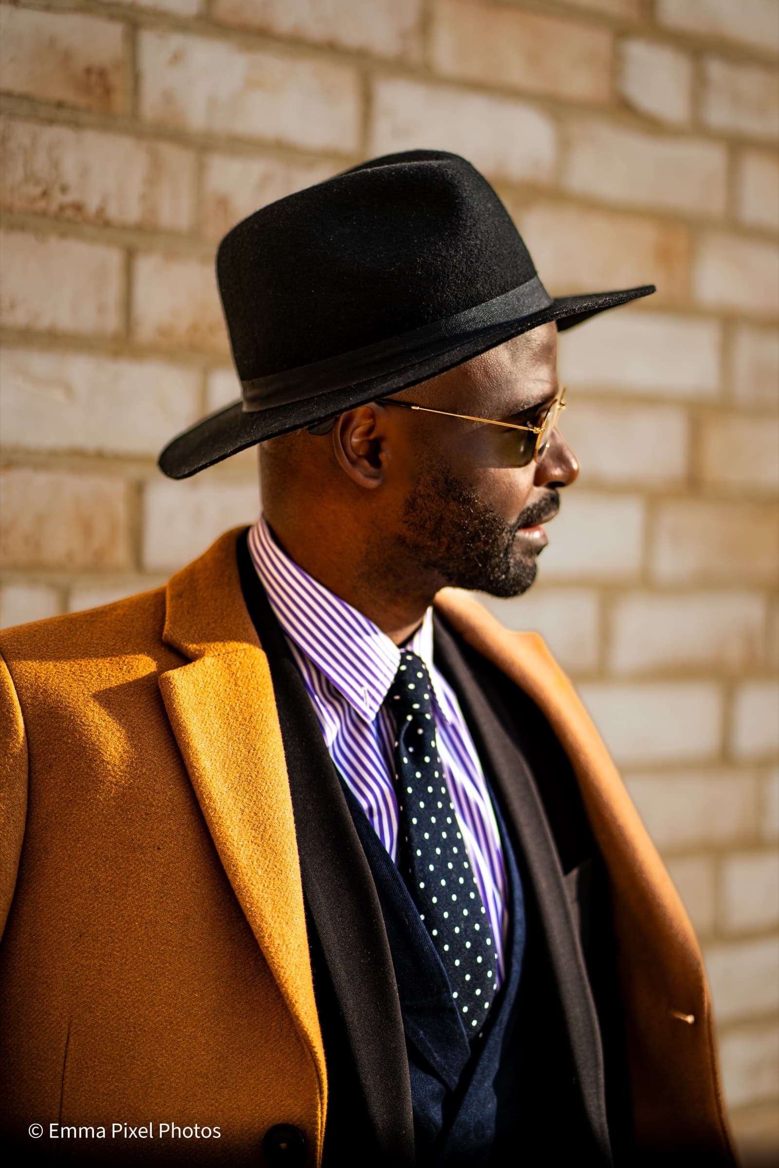 Side profile, gold sunglasses, mustard coat against brick