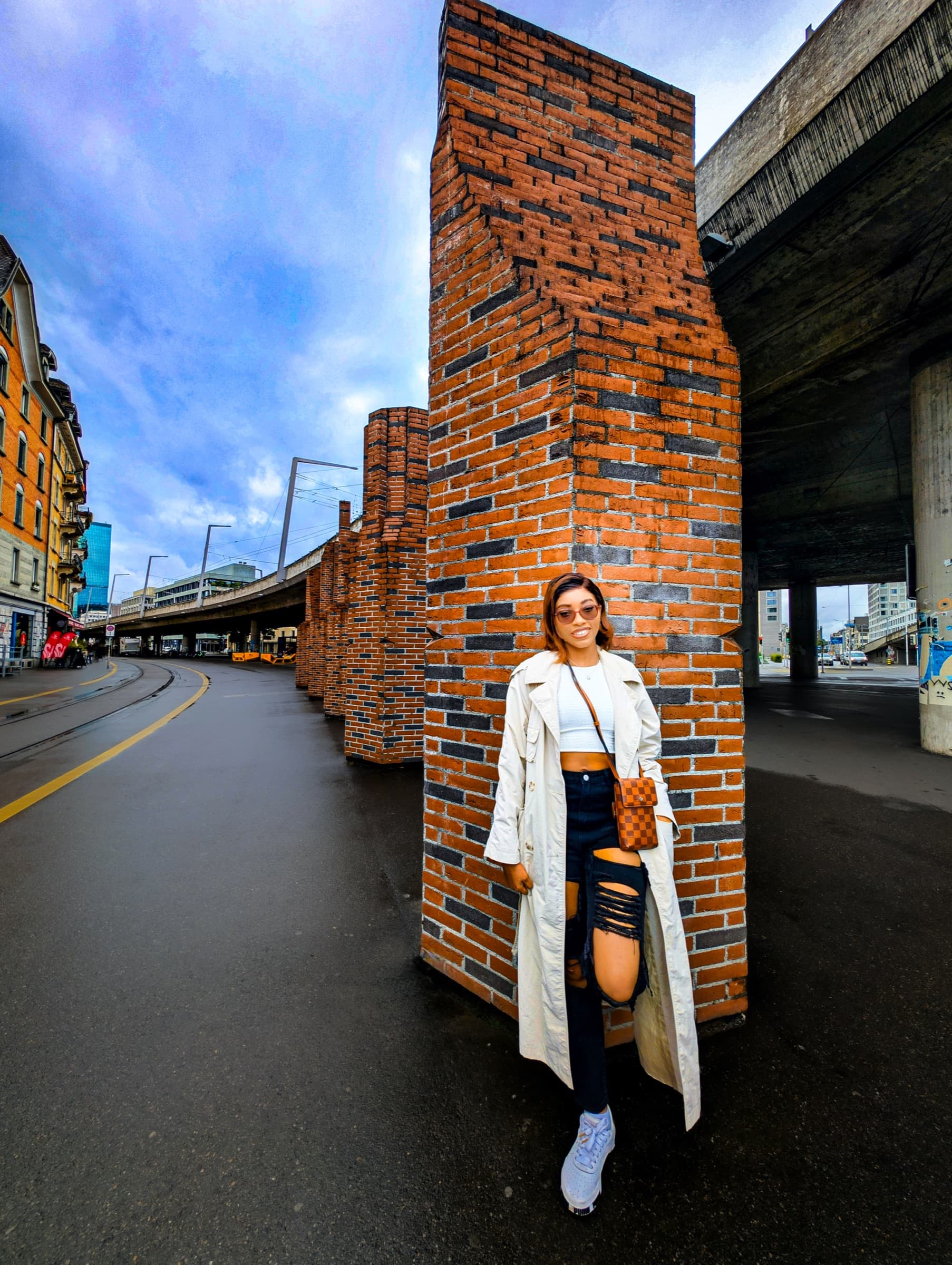 White trench coat by a brick column, urban viaduct backdrop